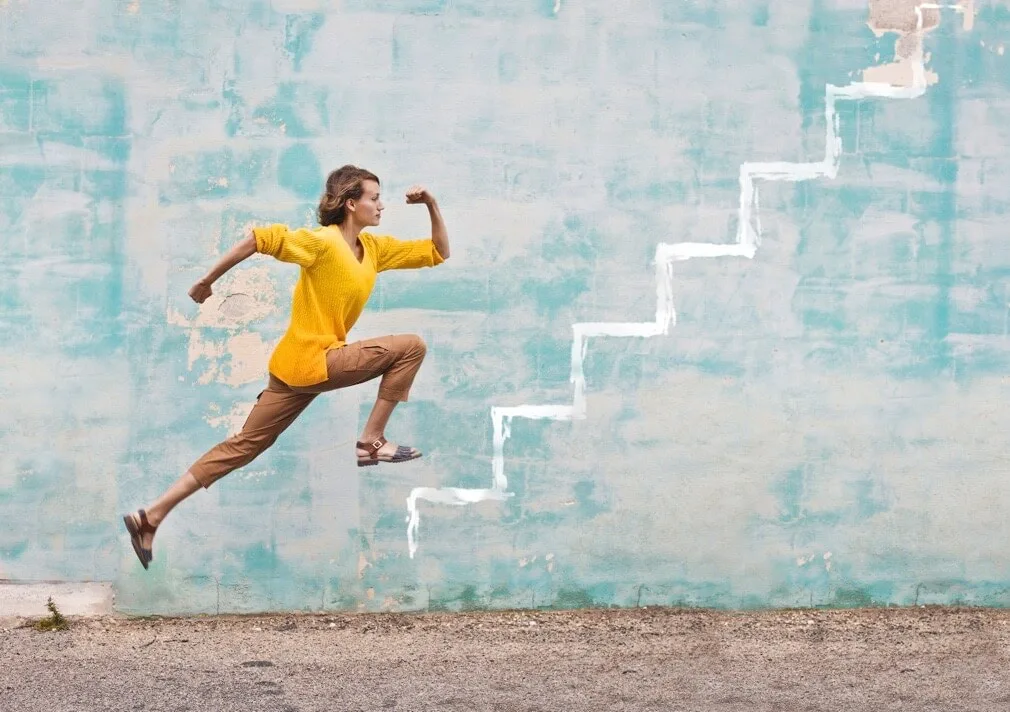 A woman runs up imaginary steps on a wall.