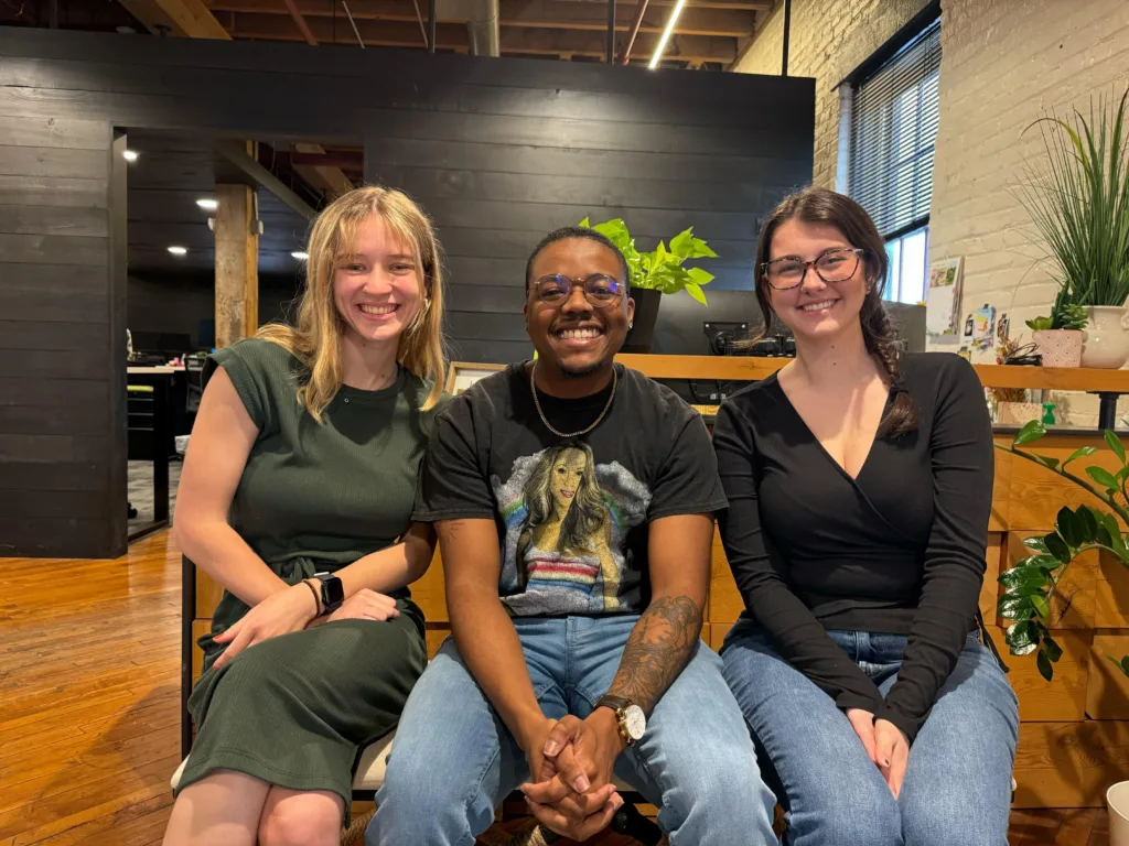 three people sitting on a bench, smiling.