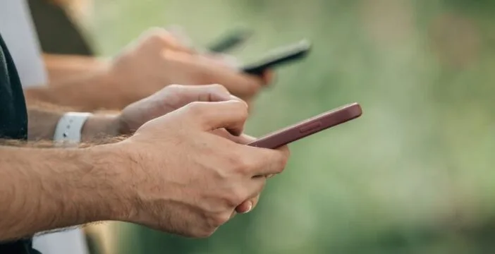 Three people stand in a row, typing on their phones.